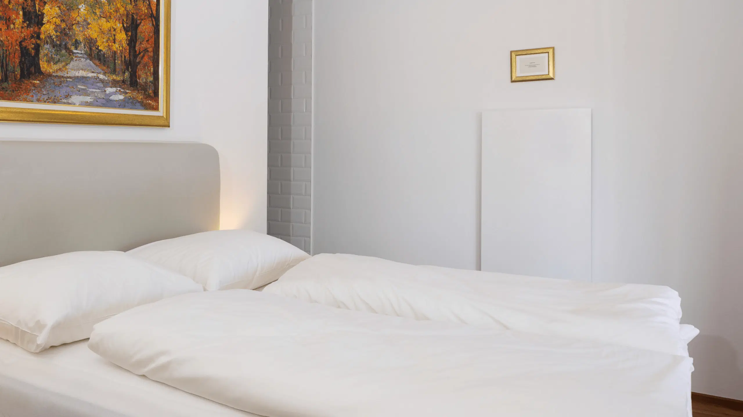Ein helles Schlafzimmer mit einem gemütlichen Bett, dekoriert mit einem Gemälde und einem kleinen Rahmen an der Wand.